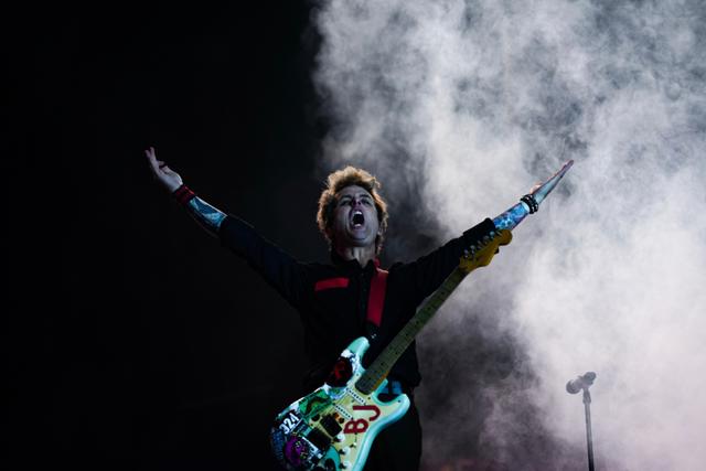 A musician with a colorful guitar stands on stage with arms raised, surrounded by smoke © Eva Manhart, All rights reserved