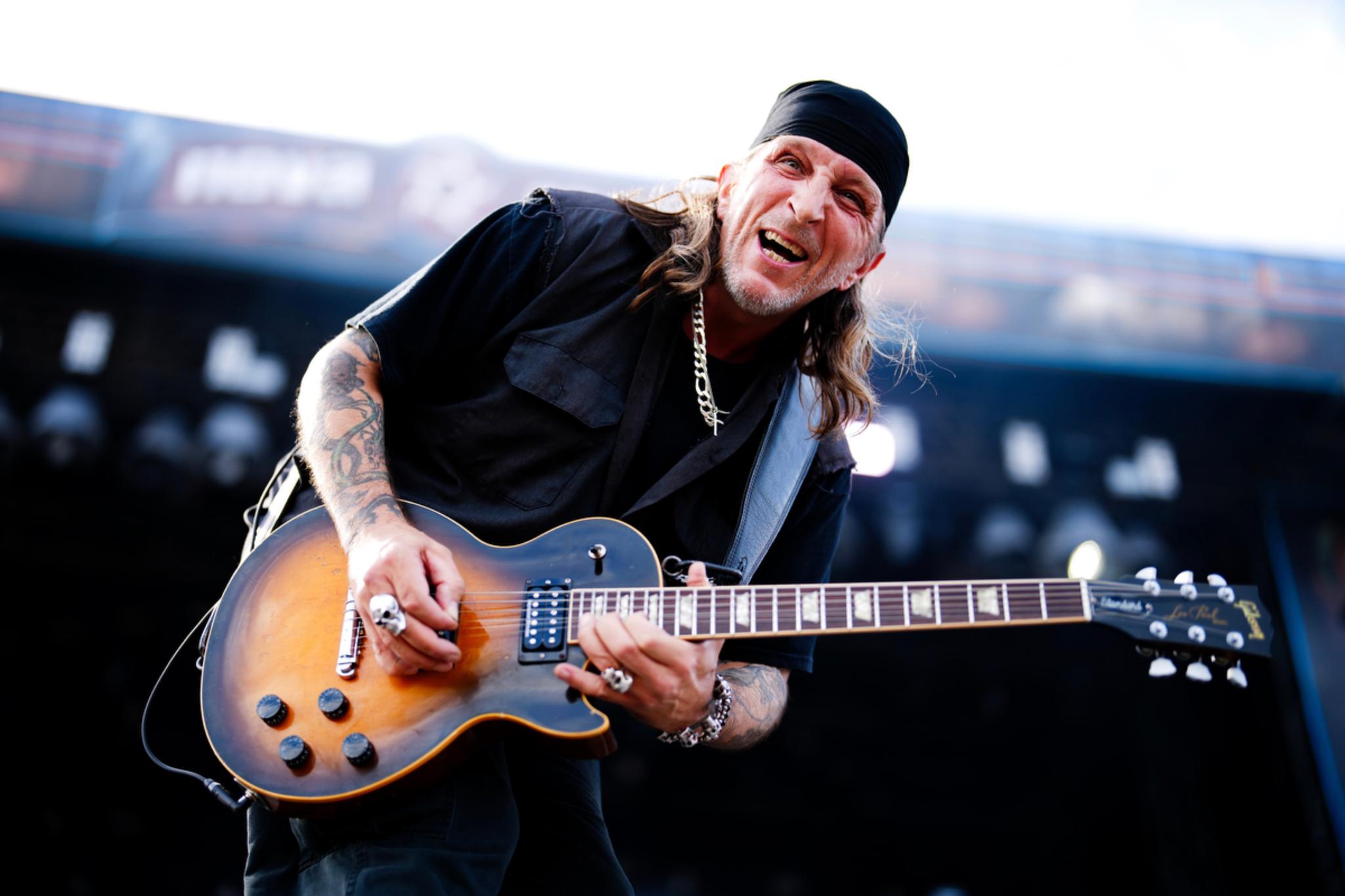 A musician with long hair and a black bandana passionately playing an electric guitar on stage