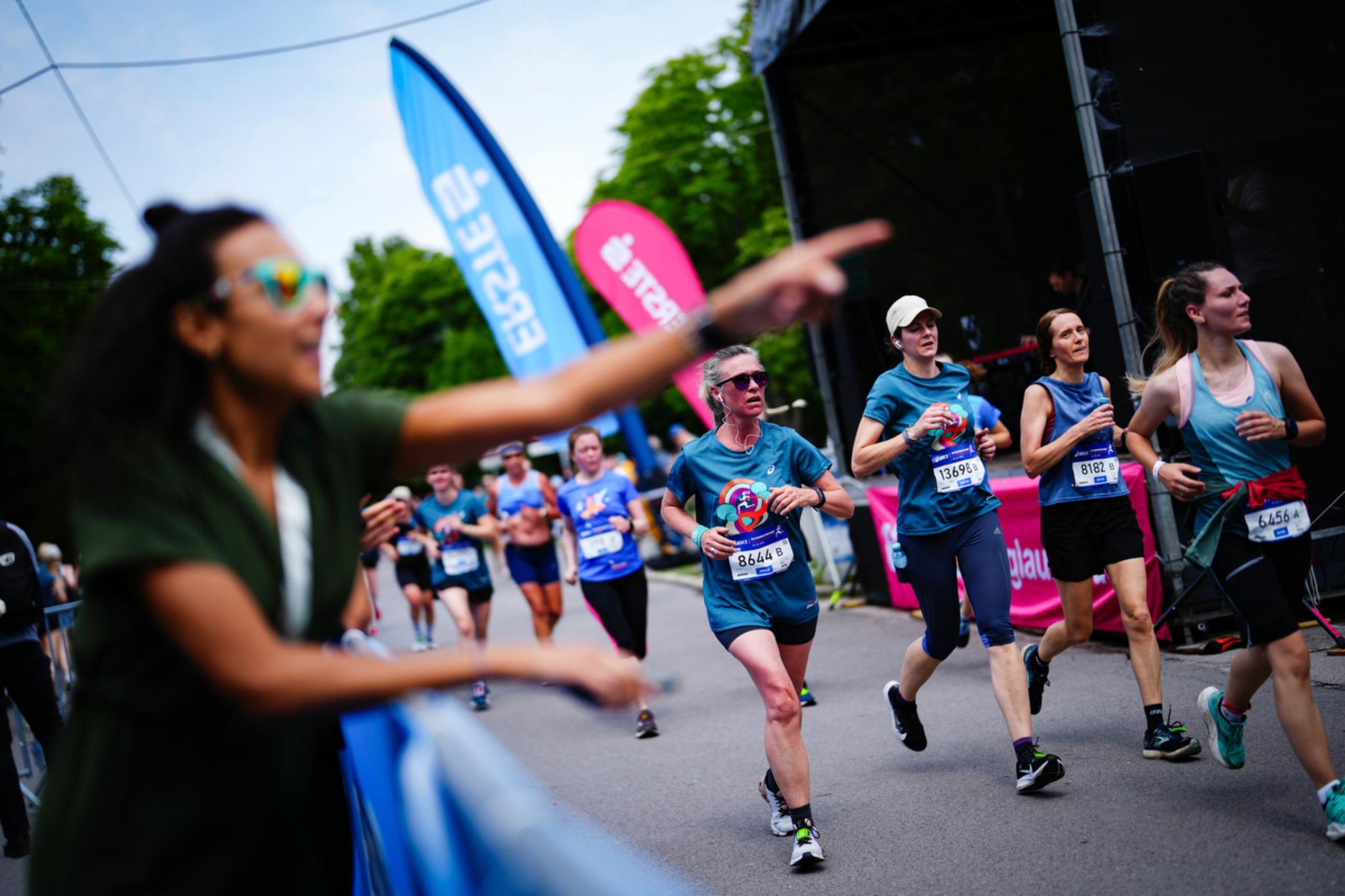 A group of runners participating in a race, with a spectator in the foreground enthusiastically pointing and cheering them on © Eva Manhart, All rights reserved