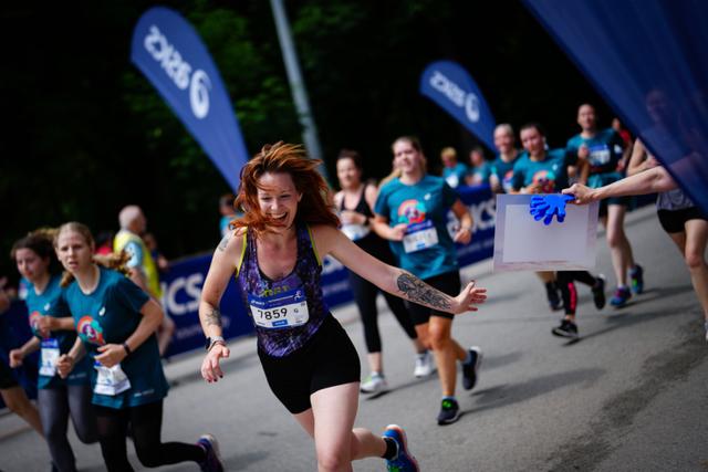 A group of runners participating in a race, with one woman in the foreground smiling and running energetically Blue banners and other participants are visible in the background © Eva Manhart, All rights reserved