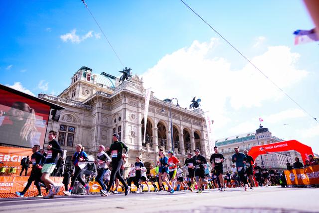 A group of runners participating in a race in front of a grand, historic building with ornate architecture under a bright blue sky © Eva Manhart, All rights reserved