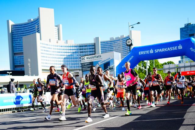 Runners participating in a marathon, passing under a blue archway with tall UNO city buildings in the background