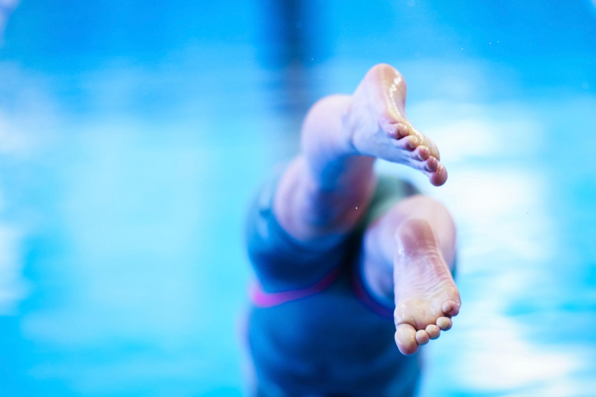 A person diving into a pool, with their legs and feet in focus against a blurred blue background © Eva Manhart, All rights reserved