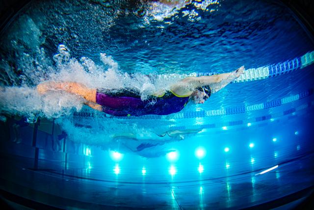 A swimmer underwater in a pool, captured mid-stroke with bright blue lights illuminating the scene © Eva Manhart, All rights reserved