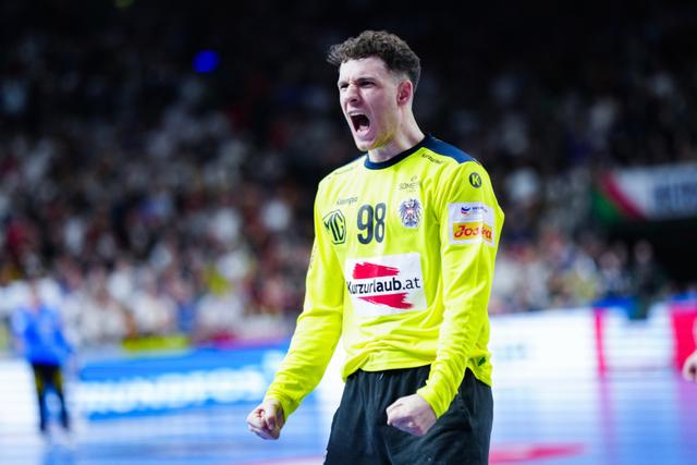 Handball player Constantin Möstl in a yellow jersey, displaying an intense expression with clenched fists, likely celebrating or reacting passionately during a game The background shows a blurred crowd and other players © Eva Manhart, All rights reserved