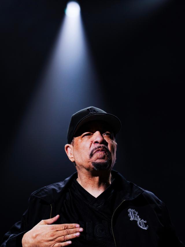 Performer and rapper Ice-T wearing a black cap and jacket stands under a spotlight, with his hand placed on his chest © Eva Manhart, All rights reserved