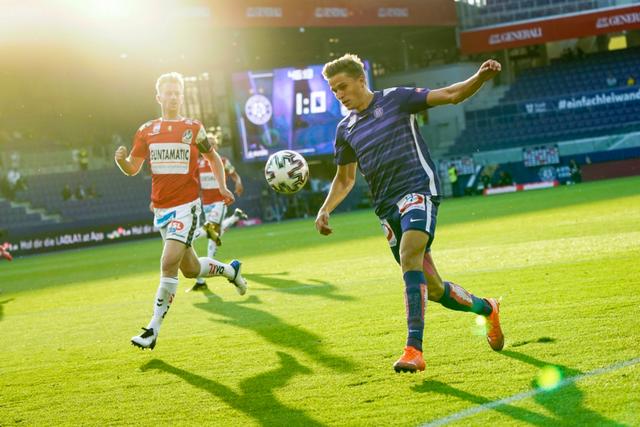 Two soccer players in action on a sunlit field, with one player in a red and white uniform and the other in a blue and white uniform © Eva Manhart, All rights reserved