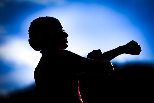 A silhouette of a person stretching their arm against a bright blue sky background