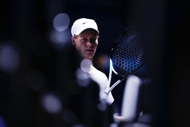 Tennis player Jannik Sinner wearing a white cap and shirt, holding a racket, with a dark, blurred background © Eva Manhart, All rights reserved