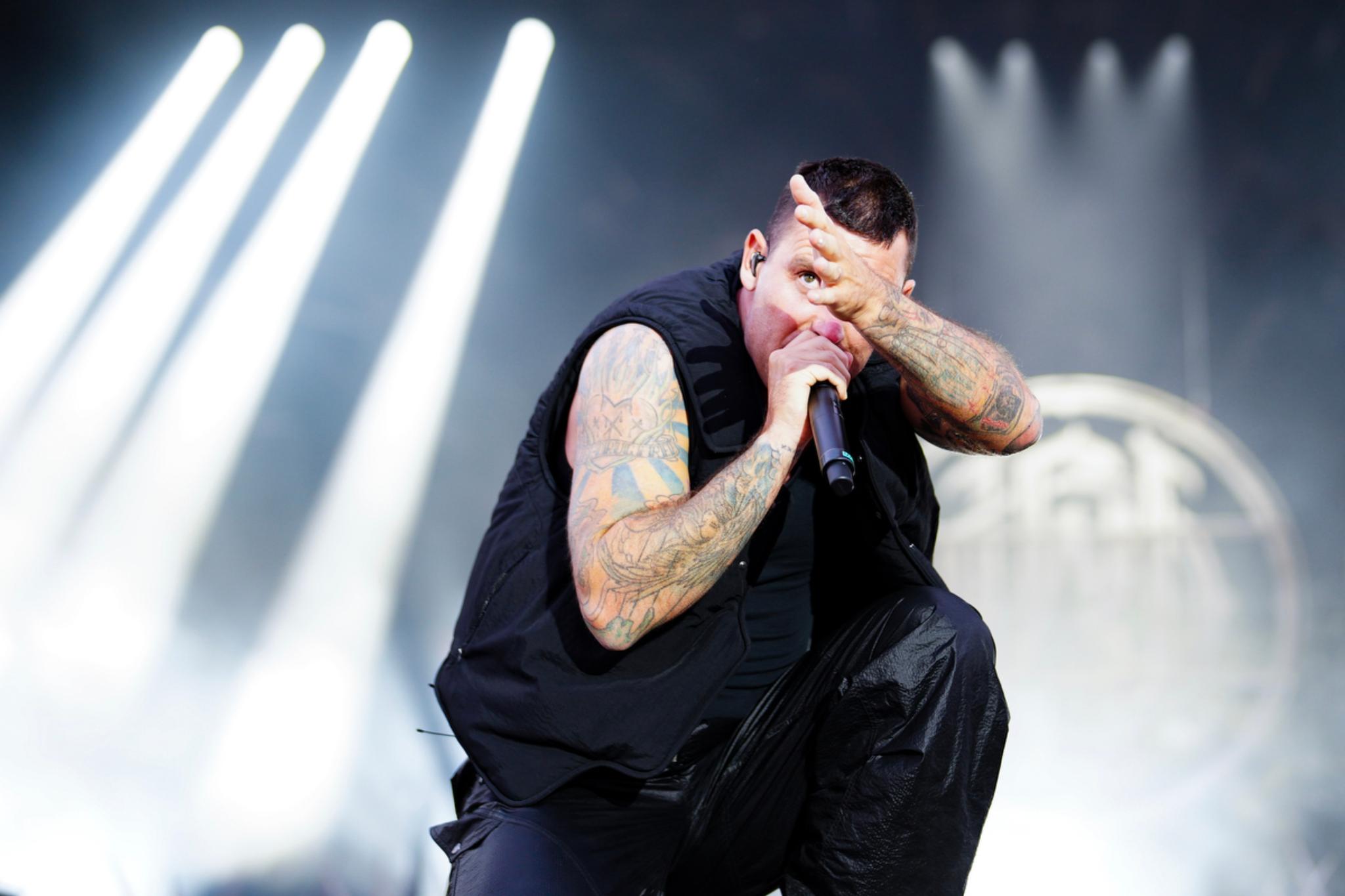 The tattooed performer Winston McCall passionately singing into a microphone on stage, with dramatic lighting and a blurred background