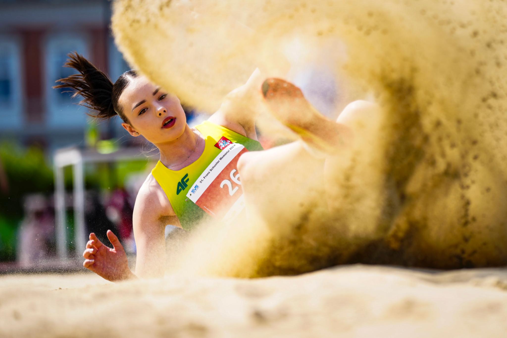 An young athlete landing in a sandpit during a long jump, with sand flying around them