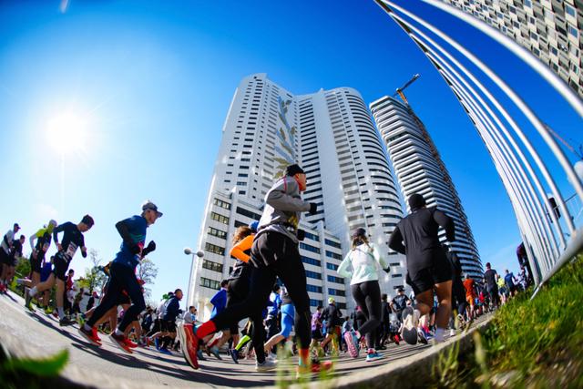 A group of people running in the Vienna city marathon with tall buildings and a clear blue sky in the background